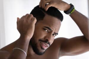African American man examines his hairline in the mirror, pleased with the improved results after DHI.